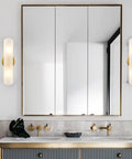 Bathroom with modern brass wall sconces two light cylinders frosted glass vanity lights on each side of mirror.