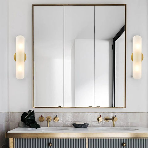 Bathroom with modern brass wall sconces two light cylinders frosted glass vanity lights on each side of mirror.