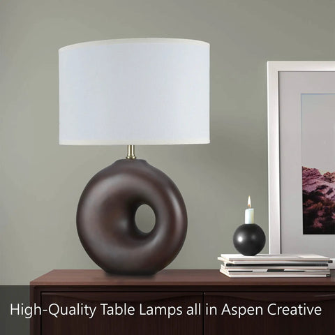 Round modern table lamp with dark brown sculpted base and white cylindrical shade on a desk with decorative accents.