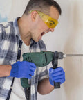 Side view of green SDS Plus rotary hammer drill with long masonry bit in use by a person wearing yellow safety goggles
