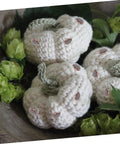 Crocheted white pumpkins with green stems and embellishments surrounded by green foliage, displayed in a decorative setting.