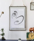 Minimalist wall art "Mom Loves You" with abstract face print in frame, on a shelf with decor including a rhino statue and clock.