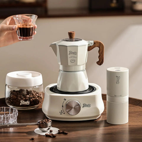 Stovetop Espresso Maker With Double Valve Tech Italian Moka Pot brewing coffee on an electric stove with two mugs.