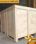 Pallet puller clamp, orange steel, in front of a large wooden shipping crate.