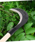Grass Scythe With Manganese Steel Blade And Long Handle For Easy Weeding And Lawn Care, shown cutting through green foliage.