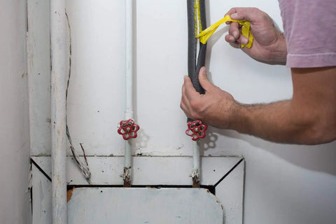 Person installing insulating foam pipe covers 0.75 inch by 3 feet pack of 4 sticks self sealing pre slit on pipes in utility room.