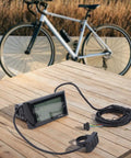 Versatile LCD Display Meter Panel For Electric Bikes And Ebikes on wooden table near bicycle, showing screen and connectors