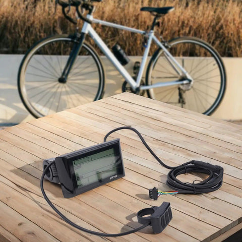 Versatile LCD Display Meter Panel For Electric Bikes And Ebikes on wooden table near bicycle, showing screen and connectors