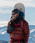 Man using Push To Talk Handheld And Wearable Speaker Microphone Set For GMRS Radios, with snowboard, in snowy mountain setting