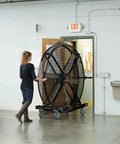 A person moving a 6 foot industrial mobile floor fan with OSHA certified safety cage wheels in a large workspace.
