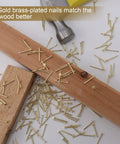900 Piece Brass Plated Finishing Nails 3 4 Inch By 17 Gauge Flat Head Carbon Steel Fasteners scattered on wood surface.
