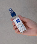 ZEISS lens cleaner spray bottle, 2 oz, blue nozzle, held in hand