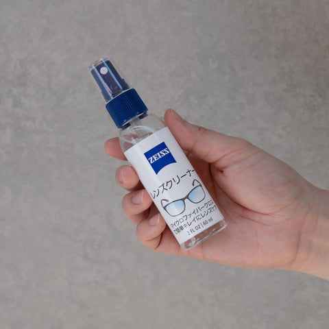 ZEISS lens cleaner spray bottle, 2 oz, blue nozzle, held in hand