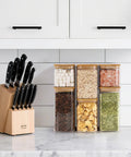 Six Pack Airtight Glass Storage Canisters With Square Lids Set For Flour Cereal Sugar Tea Coffee Beans Snacks Pantry Organization Kitchen Jars 0.7 Qt 1.2 Qt 1.6 Qt filled with food items on a kitchen counter alongside a knife block.