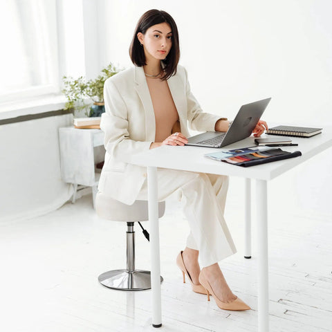 Woman working at desk on adjustable vanity stool with 360 degree swivel white faux leather makeup chair, home studio setup