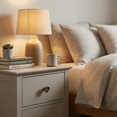 Bedroom scene with antique brass heart cabinet knobs with hammered texture solid metal drawer pulls on a nightstand beside a bed.