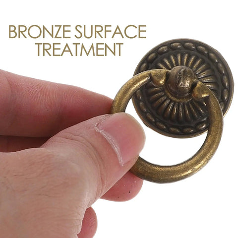 Close-up of a vintage ring pull handle in antique bronze finish with detailed design and hand holding it, part of an 8-pack for cabinets.