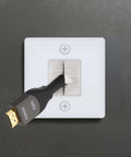 Front view of white hole-saw wall plate with brushed metal brush insert; HDMI cable partially inserted