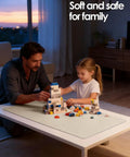 Father and daughter playing with building blocks on a white table at sunset in a cozy living room scene.