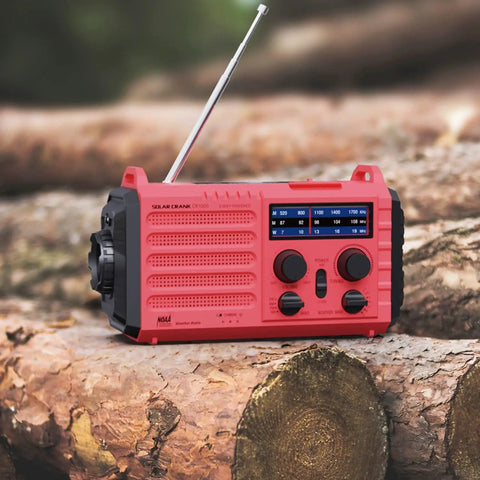 Red NOAA Weather Radio With Battery Backup And Solar Hand Crank, Portable AM FM Shortwave Receiver on logs outdoors