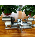 Compact Mini Metal Lathe For Benchtop Use With 3 Jaw Chuck And Tailstock on wooden surface with plants, showcasing durable all-steel construction.