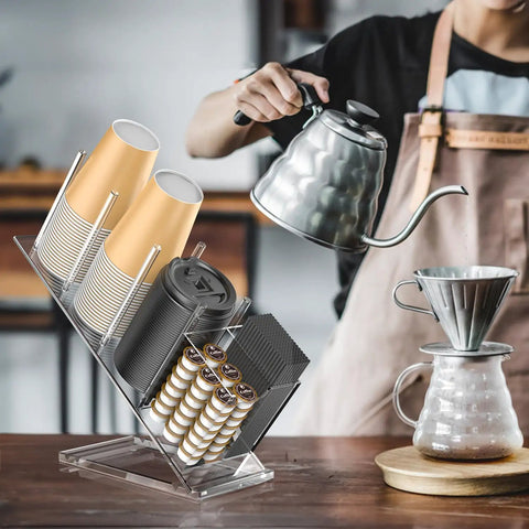 Clear Acrylic Cup And Lid Holder With Straw Organizer Adjustable Five Compartment Cup Dispenser For Disposable Paper And Plastic Cups The No Fuss Countertop Organizer For Your Home Kitchen with coffee brewing in the background.
