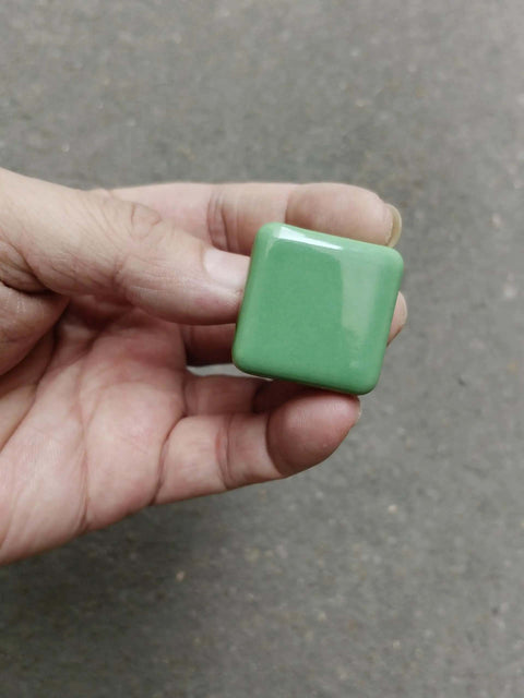 Hand holding glossy ceramic square cabinet knob, 1.25 inch green, six pack, kid friendly, with three size screws easy install