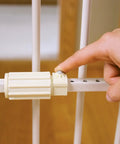 Close-up of hand adjusting pressure mount on No Drill Pressure Mount Metal Dog Gate For Doorways And Hallways Expandable From 22 To 38 Inches 18 Inches Tall White Indoor Gate With Small Pet Door Easy Setup Rust Resistant And Wall Friendly For Stairs And Openings.
