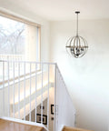 Harmon 27 Inch Six Light Dope Modern Farmhouse Armillary Chandelier With Sphere Globe Design In Smoked Birch Finish hanging above staircase