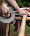 Person using Ferociously Strong Duct Tape One Point Eight Eight Inch By Thirty Five Yard Dark Gunmetal Gray One Roll With Premium Adhesive UV Resistant for repairs on a wooden pole outdoors.