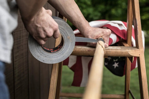Person using Ferociously Strong Duct Tape One Point Eight Eight Inch By Thirty Five Yard Dark Gunmetal Gray One Roll With Premium Adhesive UV Resistant for repairs on a wooden pole outdoors.