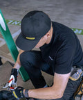 A person wearing a Rainier BCX Bump Cap Made In USA With Low Profile Protection And Ball Cap Style Vibe, Snap Back Closure, in black.