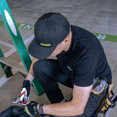 A person wearing a Rainier BCX Bump Cap Made In USA With Low Profile Protection And Ball Cap Style Vibe, Snap Back Closure, in black.