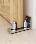 Close-up of wall-mounted stainless steel barn door floor guide set, flush bottom design, installed on light wood floor; Barn Door Floor Guide Set Of 2, Stainless Steel Adjustable Wall Mounted Floor Guide For Doors Up To Two And One Eighth Inches Thick, Flush Bottom Design For Floor Friendly Finish, Smooth And Quiet Roller Operation, Super Easy Install.