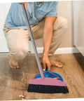 A person using a Heavy Duty Pink Broom With Extended Handle Sweeps Indoors And Outdoors, cleaning hardwood floor.