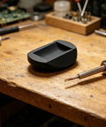 Black object on wooden table near soldering iron, workshop setting