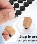 Hand applying Lock Tight Adhesive Felt Pads For Furniture Legs 312 Pack Round Cabinet Bumpers to wooden furniture leg.