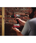 Person using 20V Max Cordless Drill Driver Kit with Two Batteries and Charger, One Half Inch Chuck on a wooden frame against a brick wall.