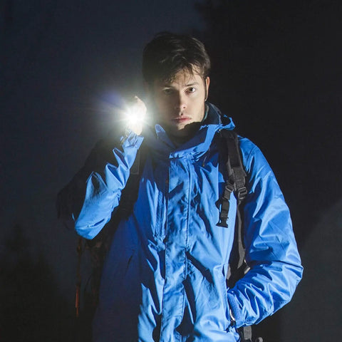 Person using 12 Pack Mini LED Pen Flashlights With Clip, compact flashlight illuminating path at night, wearing blue jacket.