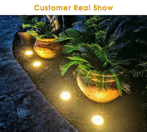 Lit 16 LED Solar Ground Lights Outdoor Warm White Disk Lights illuminating a garden path with potted plants at night.
