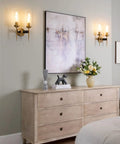Two-Light Gold Brass Wall Sconces with 2.8 Inch Cylindrical Clear Glass Shades, E26 Base, in a bedroom setting on pale wall.