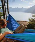 Person relaxing in Neolite Single Camping Hammock Ultra Lightweight Portable Nylon Parachute Hammock by lakeside, sky blue color.