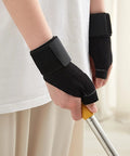 Person wearing Reversible Thumb And Wrist Stabilizer Splint Brace For Trigger Finger Pain Relief, holding a tool, lightweight black.