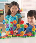 Children playing with Gears 100-Piece Deluxe Building Set For STEM Fun, Fine Motor Play And Creative Discovery on a table.
