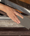 Person using Premium Alipis 45 Sheets Waterproof Sandpaper For Wood And Leather Work on a wooden surface.