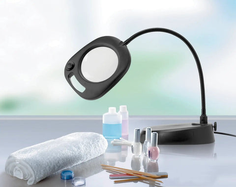 Go-To LED Floor Lamp And Table Lamp With 5-Inch Magnifier on a salon table with beauty products, flexible arm visible, sleek black design.