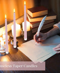 Person writing near pink 11-inch LED flickering flameless taper candles with books, showing realistic candlelight for decor.