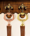 Front view of two metal wall-mounted bottle openers with circular rings in rose gold and gold finishes, wooden handles.