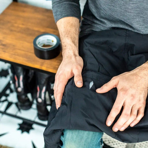 Person repairing a black jacket with Black Color Duct Tape All Purpose Heavy Duty Tape For Repairs Crafting And Imaginative Projects Totally Temporary Floor Marking Removable Up To Three Weeks Not For Hardwood Or Direct Sunlight Durable Multi Use Roll visible on table