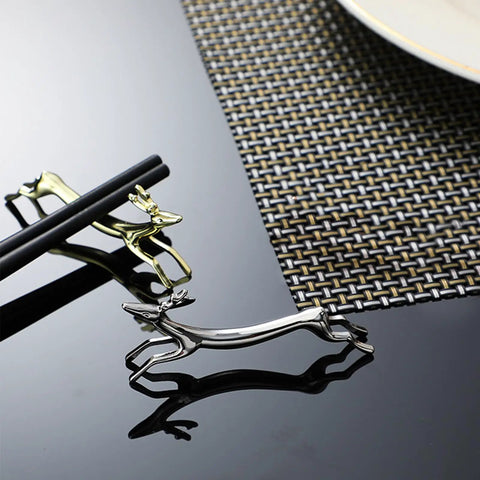 Gold and silver stainless steel deer-shaped utensil holders on a reflective black surface
